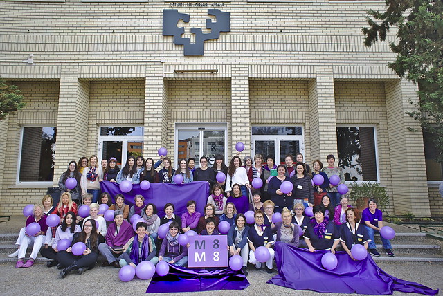 Grupo de mujeres con globos y telas moradas en las escaleras frente a la Facultad de Informática