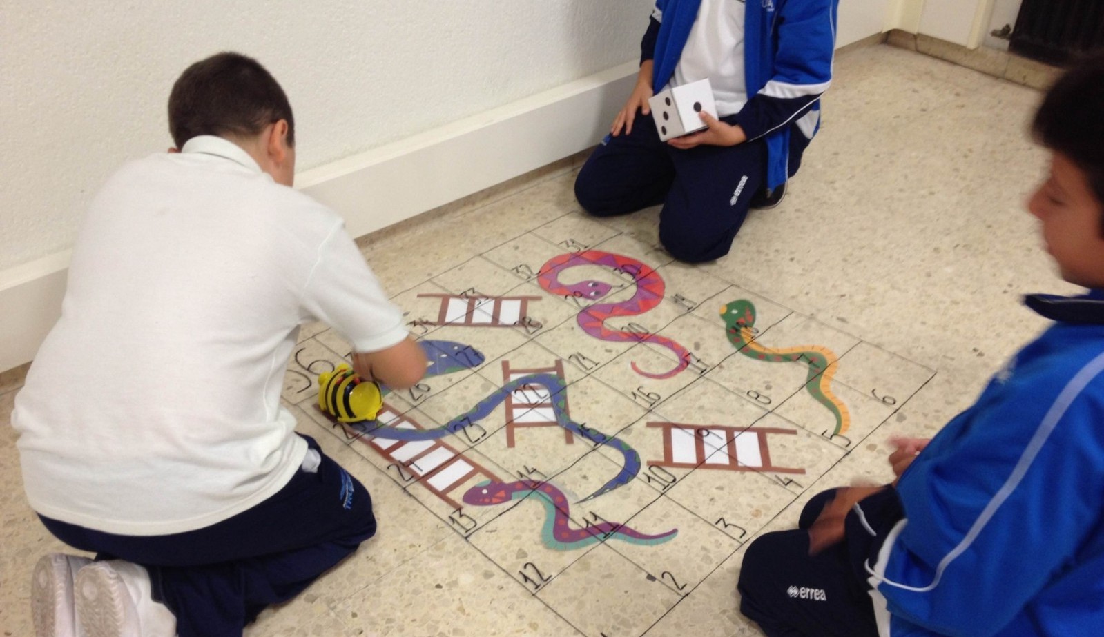 Niños juegan en el suelo a un juego de mesa con serpientes y escaleras