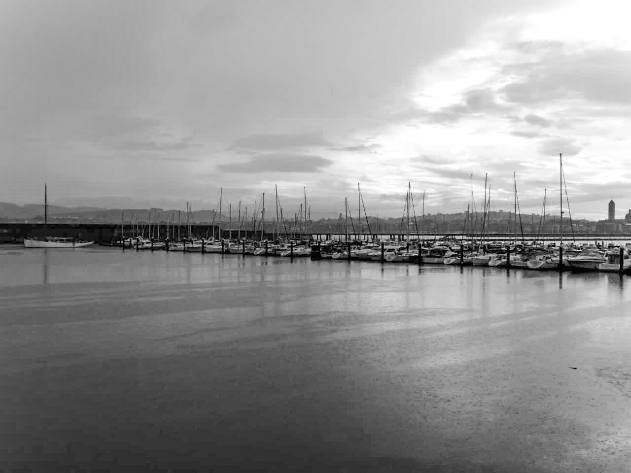 Paisaia gris bat ikusten dugu. Itsaso barean portu zabal bat, itsasontzi eta belaontzi ilara batzuk mastak zerura begira. Portua ixten duen malekoia ezkerretik abiatzen da erdiraino maila ezberdinak marraztuz. Atzealdean, hiri batek paisaia osoa inguratzen du mendi grisaxkez burututa. Gainean, zeu hodeitsu bat, irudi osoa erdizka argiztatzen duen argigunearenkin.