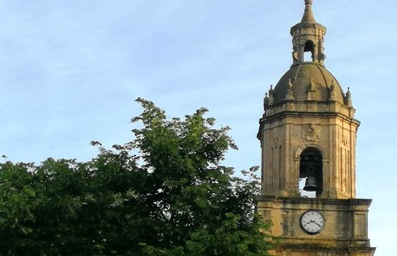 Zeru urdin dardarti baten gainean, eliza barroko baten harrizko dorrea dugu. Oinplano karratuaren gainean kanpandorre oktogonal bat, erdian arku bat duena. Bertatik kanpai beltza ikusten da, behealdean urre-koloreko lerro batekin apainduta. Dorrea, kupula batekin ixten da, oinarrian forma karratu ezberdinekin ornatuta, eta orratz batez koroatutako dorre txiki bat du goialdean. Elizaren parean, zuhaitz handi baten adaburuak irudi erdia estaltzen du.