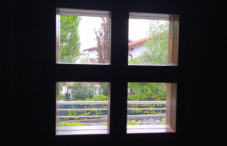 Barne beltz-beltz batetik, lautan zatituriko lehio batetik, ikusten dugu kanpoaldea. Auzo txiki bat begibistan. Lau etxe bereizten dira teilatu gorri eta horma zurikozkoak, zuhaitz berdeen artean ezkutatuta eta huntzez betetako hesi batez inguratuta. Zerua erabat grisa da, urruneko edozein paisaia arrasto ezkutatzen duelarik.